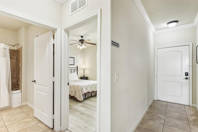 hall with light tile patterned floors, baseboards, visible vents, and crown molding