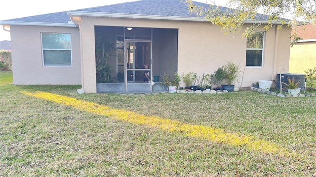 back of property with a sunroom, roof with shingles, a yard, central air condition unit, and stucco siding