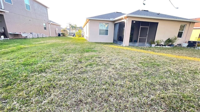 back of property with a sunroom, a lawn, and stucco siding