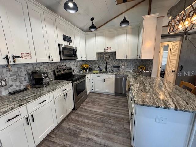 kitchen featuring stainless steel appliances, a sink, white cabinets, vaulted ceiling, and pendant lighting