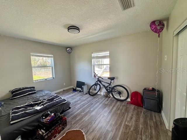 bedroom featuring visible vents, a textured ceiling, baseboards, and wood finished floors