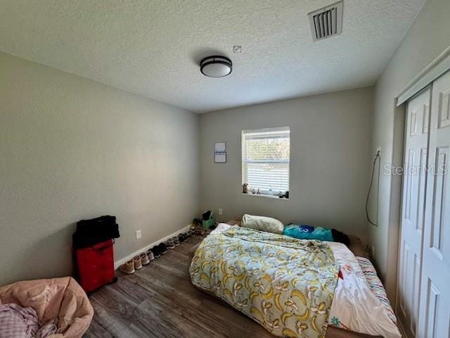 bedroom featuring dark wood-style flooring, a closet, visible vents, a textured ceiling, and baseboards