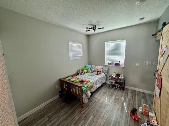 bedroom with a barn door, baseboards, and dark wood finished floors