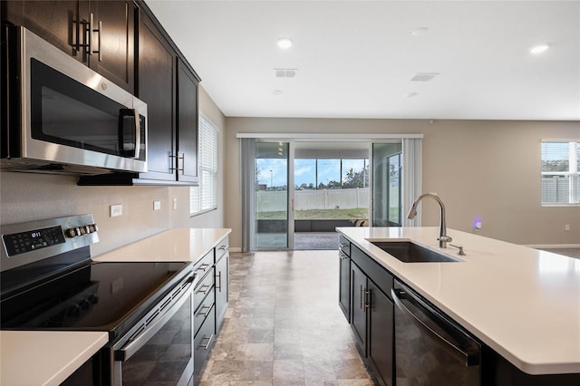 kitchen with an island with sink, appliances with stainless steel finishes, light countertops, and a sink