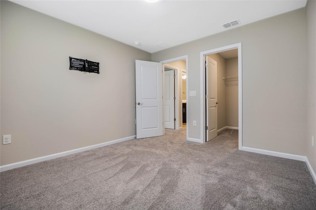 unfurnished bedroom featuring baseboards, visible vents, light colored carpet, a spacious closet, and a closet