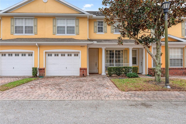 multi unit property featuring driveway, brick siding, an attached garage, and stucco siding