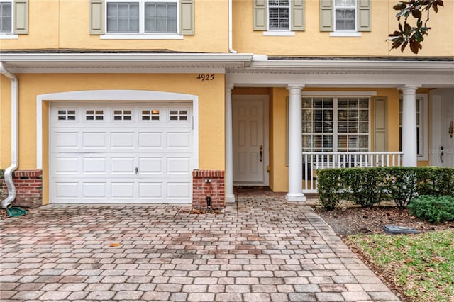 doorway to property with a garage, a porch, decorative driveway, and stucco siding