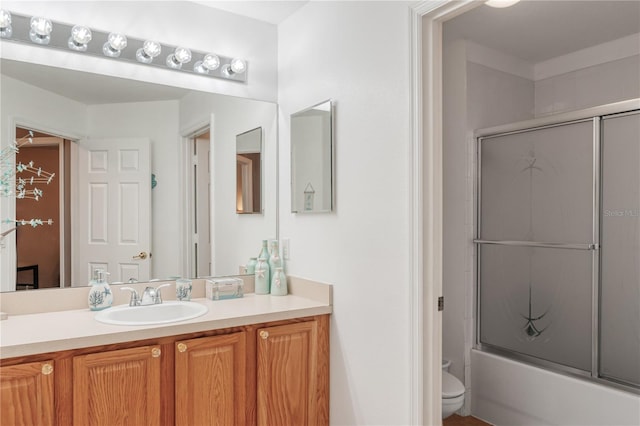 bathroom with toilet, combined bath / shower with glass door, and vanity