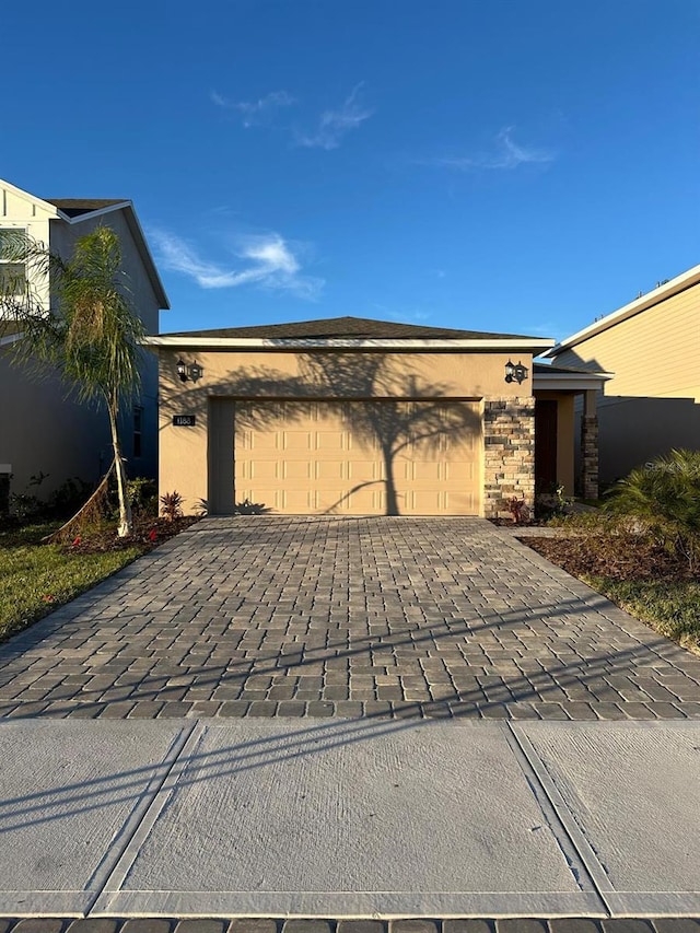 view of front of house featuring decorative driveway, stone siding, an attached garage, and stucco siding