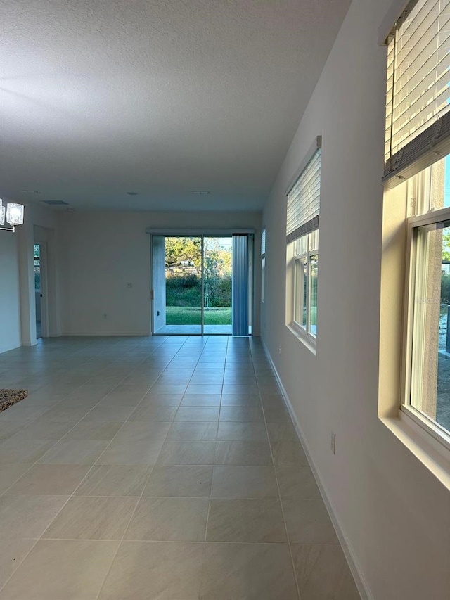 spare room featuring light tile patterned floors, baseboards, a textured ceiling, and an inviting chandelier