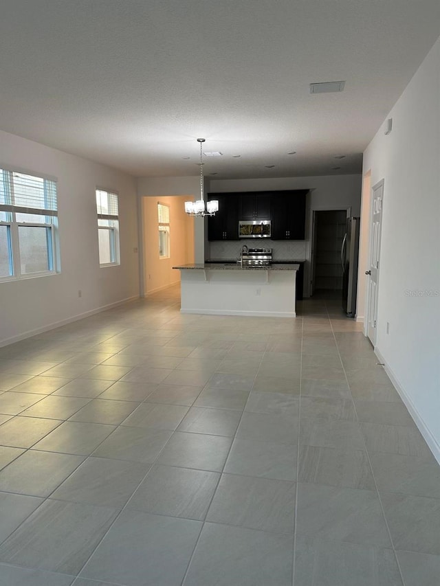 unfurnished living room with a sink, baseboards, a notable chandelier, and light tile patterned flooring