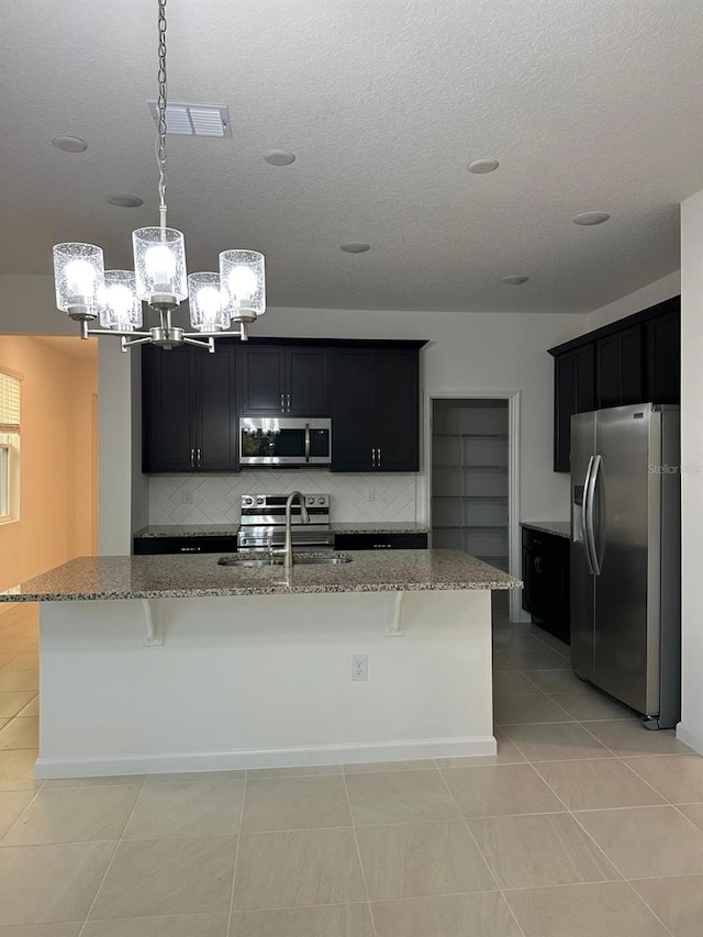 kitchen with a kitchen island with sink, stainless steel appliances, a sink, visible vents, and decorative light fixtures