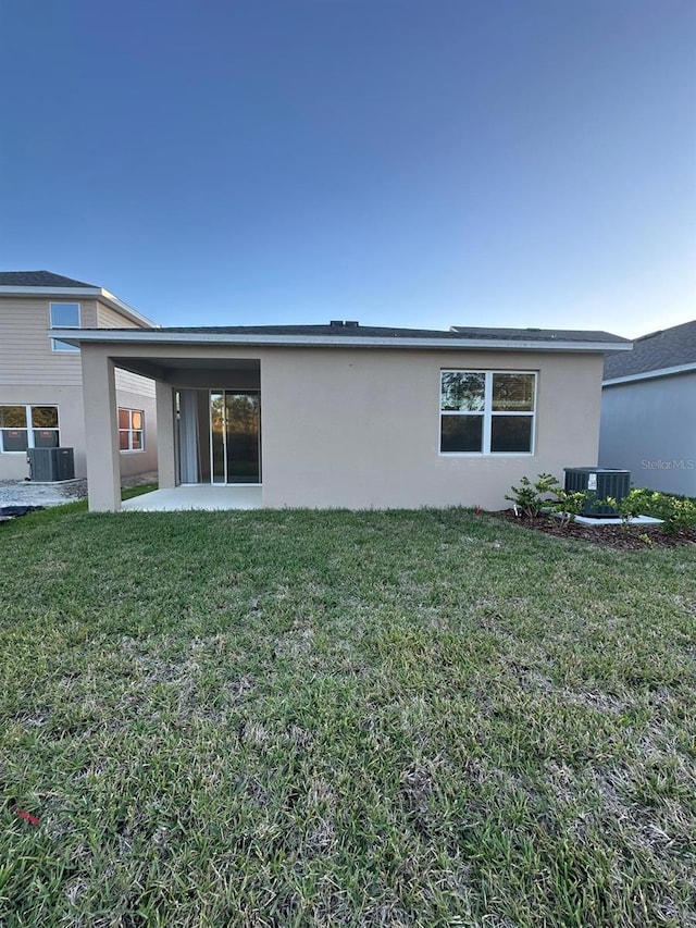 rear view of property with stucco siding, a yard, central AC, and a patio