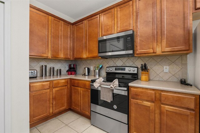 113 Tiger Lily Ct, Davenport, FL 33837 - kitchen with stainless steel appliances, light countertops, decorative backsplash, light tile patterned floors, and brown cabinetry