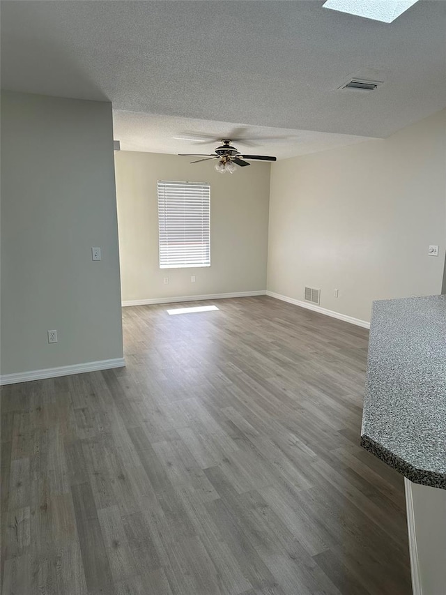 empty room featuring dark wood-style floors, a skylight, visible vents, and a textured ceiling