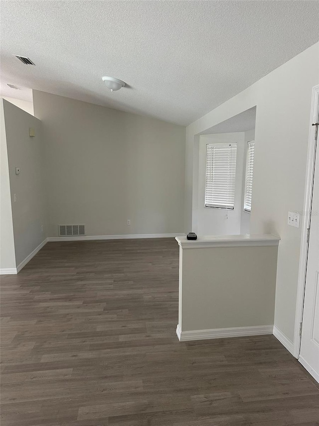 empty room featuring dark wood-style floors, baseboards, visible vents, and a textured ceiling