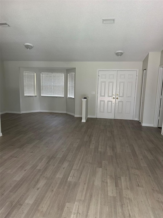 unfurnished living room with dark wood-style floors, a textured ceiling, and visible vents