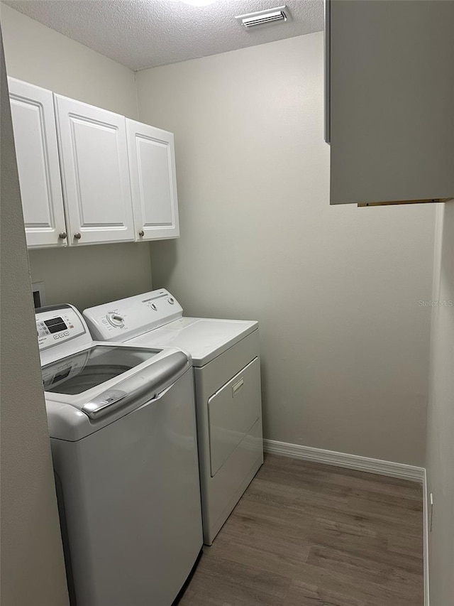 laundry room featuring a textured ceiling, separate washer and dryer, wood finished floors, visible vents, and cabinet space