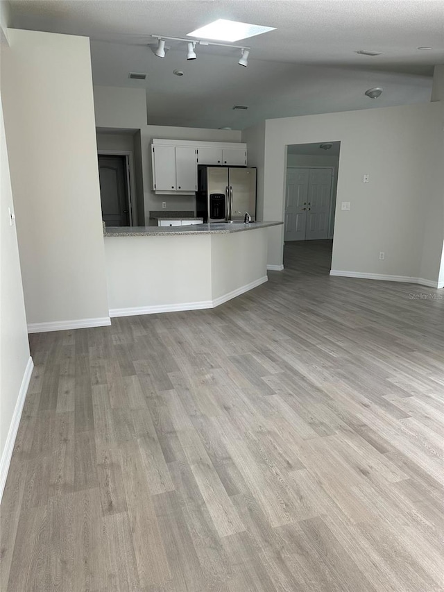 kitchen with a peninsula, light wood-style flooring, white cabinetry, and stainless steel fridge with ice dispenser