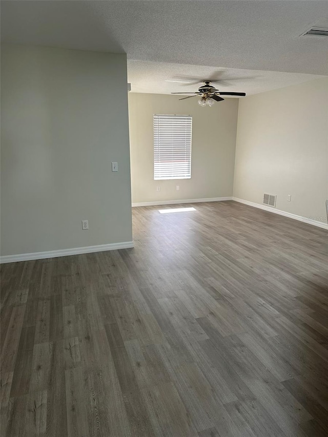 spare room with baseboards, visible vents, ceiling fan, dark wood-style flooring, and a textured ceiling