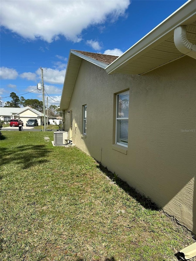 view of side of home featuring central AC, a yard, and stucco siding