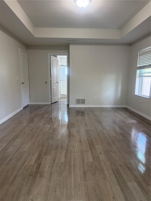 empty room with a tray ceiling, dark wood-style flooring, visible vents, and baseboards