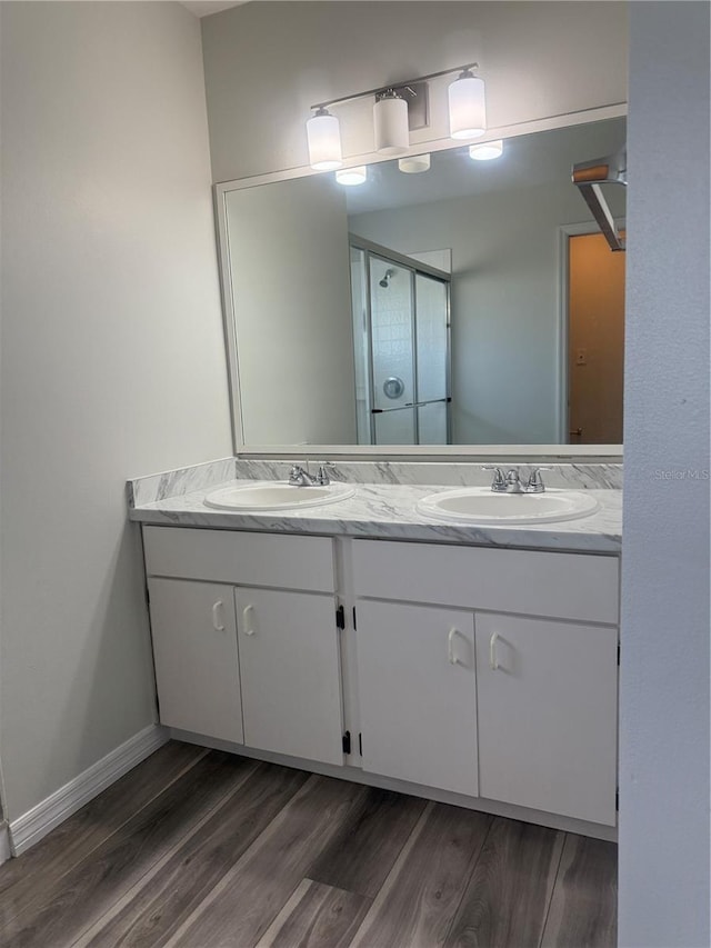 full bathroom with double vanity, wood finished floors, a sink, and a shower stall