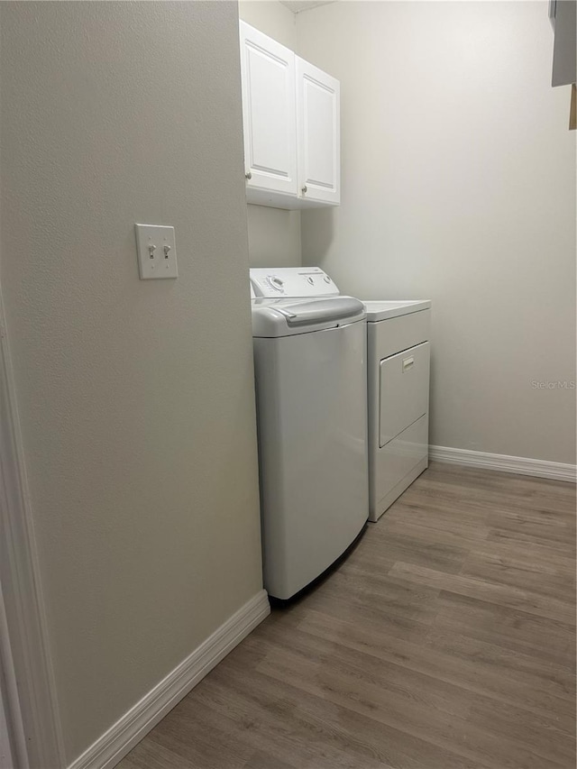 washroom featuring cabinet space, light wood-style flooring, baseboards, and washing machine and clothes dryer