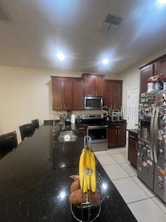 kitchen with light tile patterned floors, visible vents, dark countertops, stainless steel appliances, and a sink