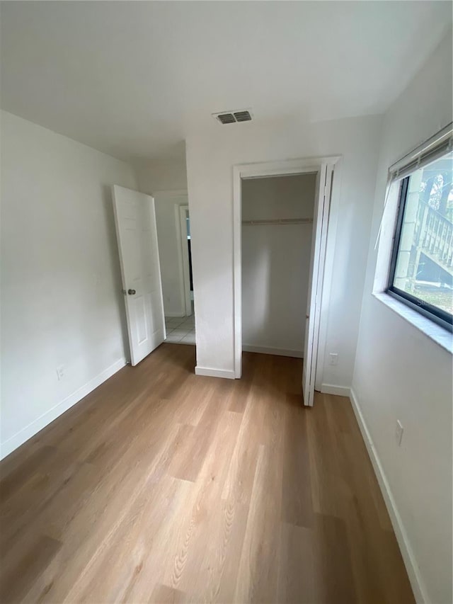 unfurnished bedroom featuring light wood-style flooring, a closet, visible vents, and baseboards