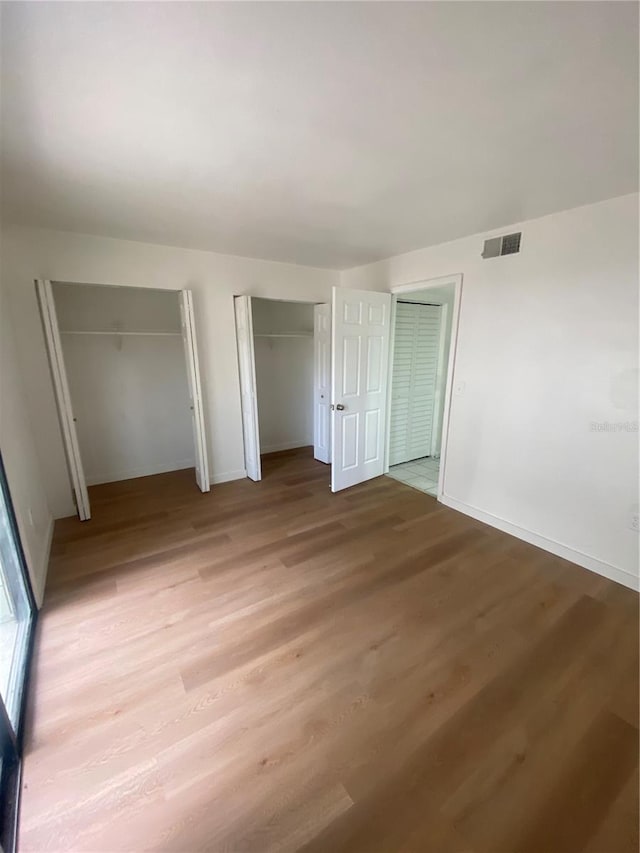 unfurnished bedroom featuring light wood-style floors, baseboards, visible vents, and two closets