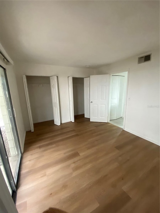 unfurnished bedroom with wood finished floors, multiple windows, two closets, and visible vents