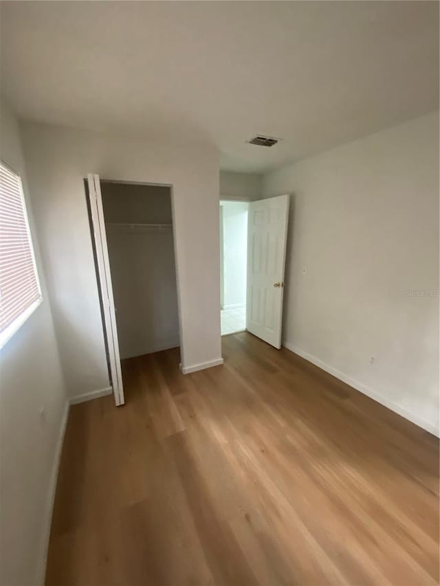 unfurnished bedroom with a closet, visible vents, baseboards, and light wood finished floors