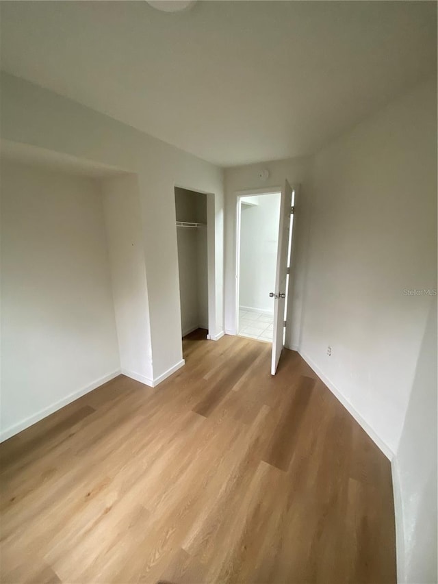 unfurnished bedroom featuring a closet, light wood-type flooring, and baseboards