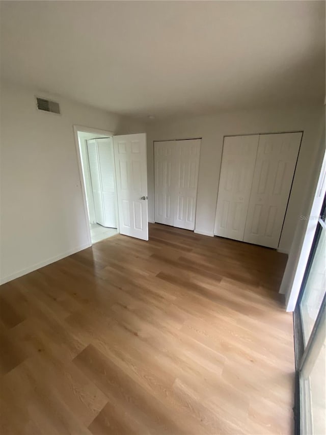 unfurnished bedroom featuring baseboards, light wood finished floors, visible vents, and multiple closets