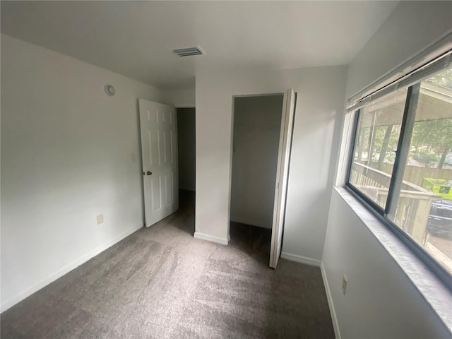 unfurnished bedroom featuring a closet, dark carpet, visible vents, and baseboards