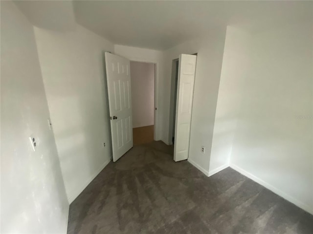 unfurnished bedroom featuring dark carpet and baseboards