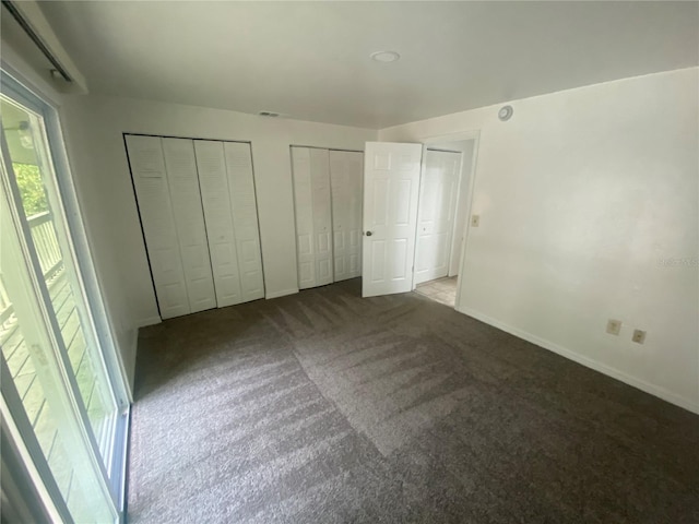 unfurnished bedroom with baseboards, carpet floors, visible vents, and multiple closets