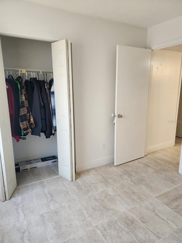 unfurnished bedroom featuring a textured ceiling, a closet, and baseboards