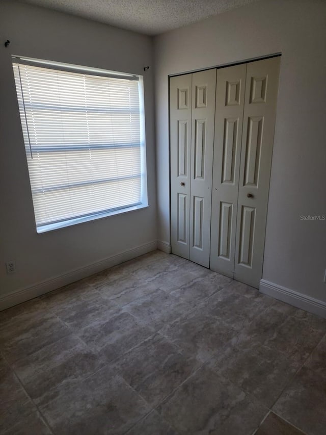 unfurnished bedroom featuring a textured ceiling, a closet, and baseboards