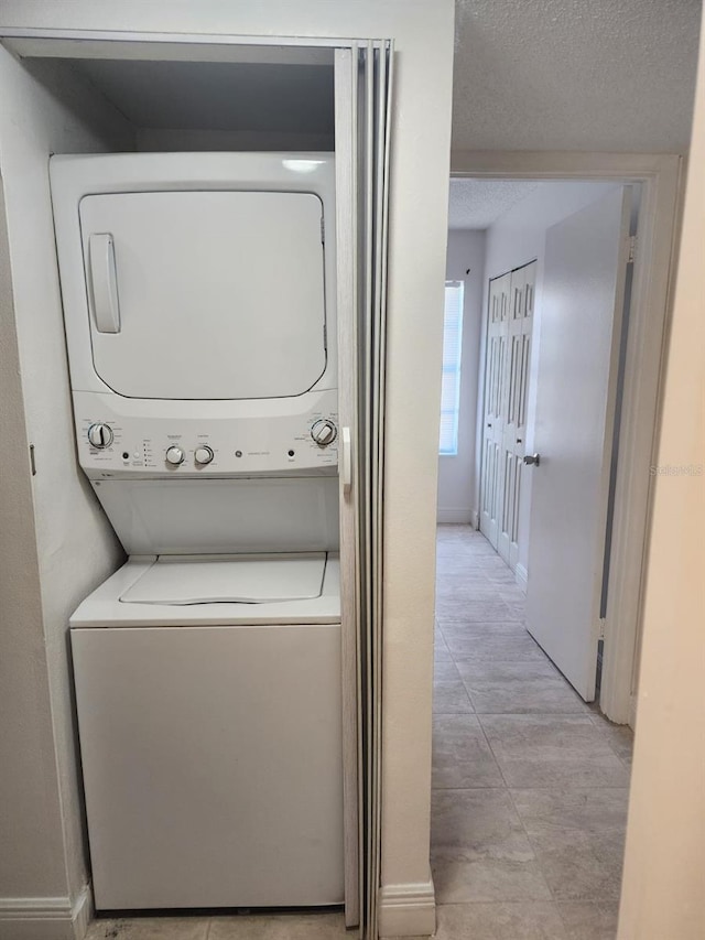 laundry area featuring a textured ceiling, laundry area, stacked washer and clothes dryer, and baseboards