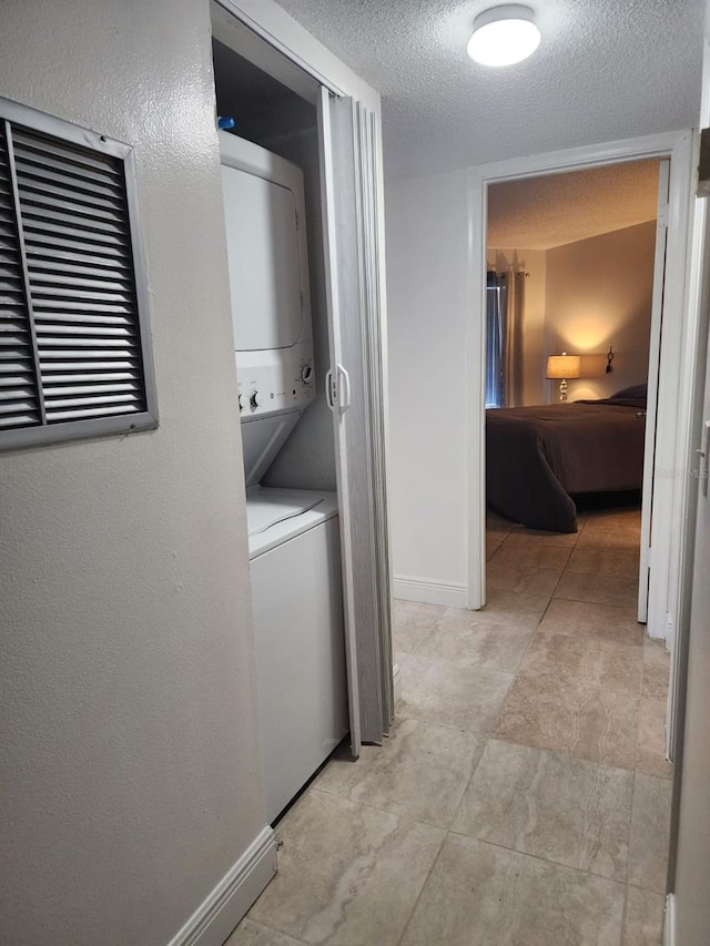 laundry area with a textured ceiling, laundry area, stacked washing maching and dryer, and baseboards