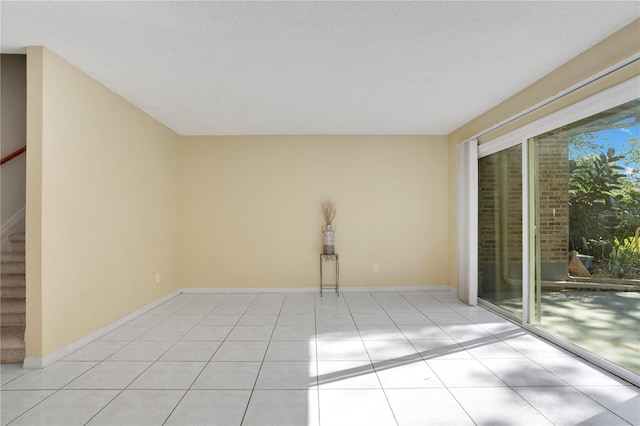 spare room with light tile patterned floors, baseboards, and stairway