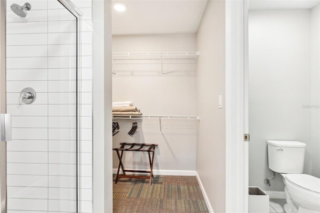 bathroom featuring toilet, a stall shower, a spacious closet, and baseboards