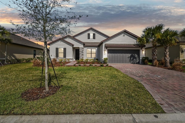 view of front of house with a garage, stone siding, decorative driveway, stucco siding, and a front lawn