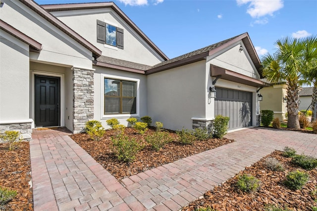 exterior space featuring stone siding, decorative driveway, an attached garage, and stucco siding