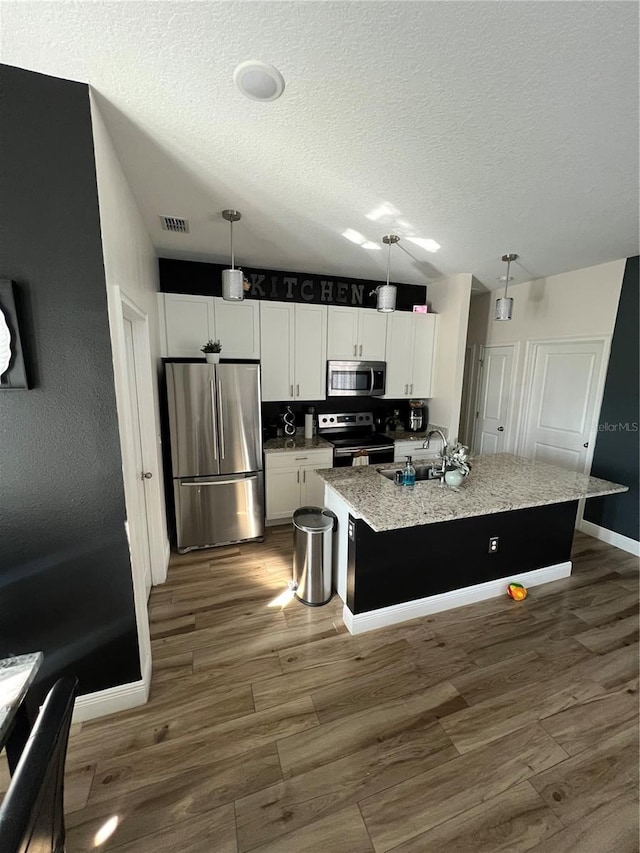 kitchen with hanging light fixtures, a center island with sink, and appliances with stainless steel finishes