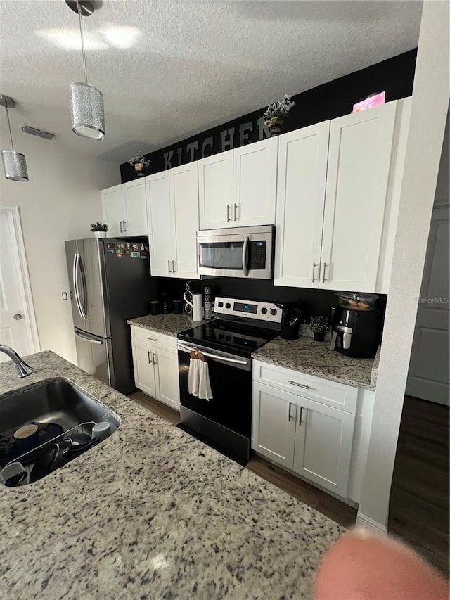 kitchen featuring visible vents, appliances with stainless steel finishes, white cabinets, and decorative light fixtures