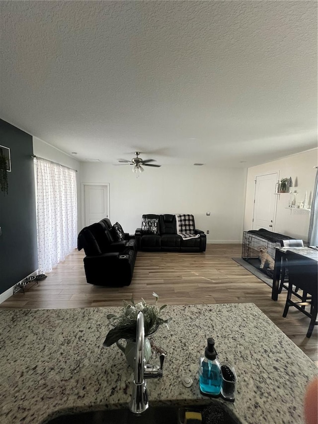 living room with ceiling fan, a textured ceiling, baseboards, and wood finished floors