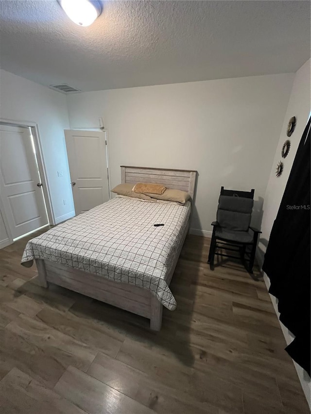bedroom featuring a textured ceiling, dark wood-style flooring, and baseboards